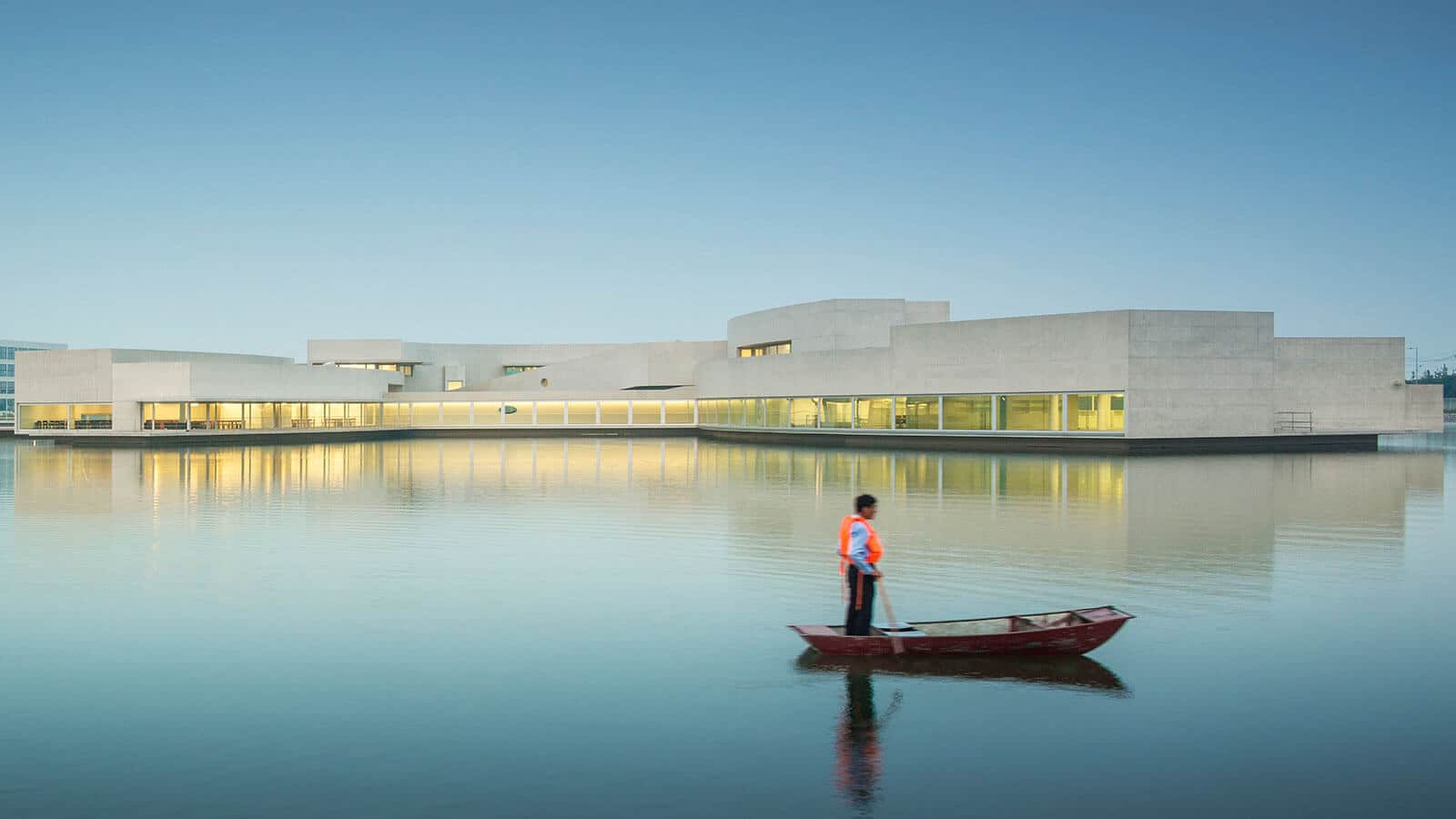 Man in a boat looks at a white concrete building.